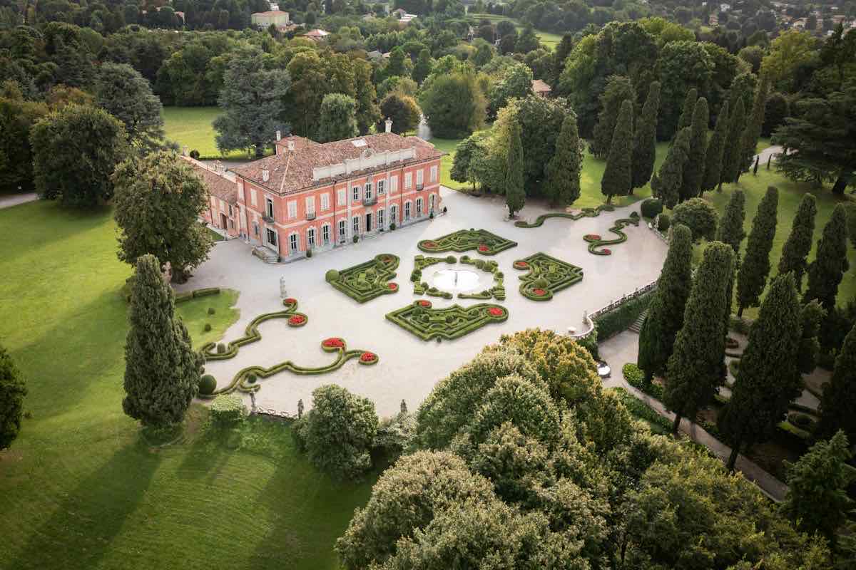 A coral-pink villa above a formal parterre of clipped hedges, among cypresses and lawns
